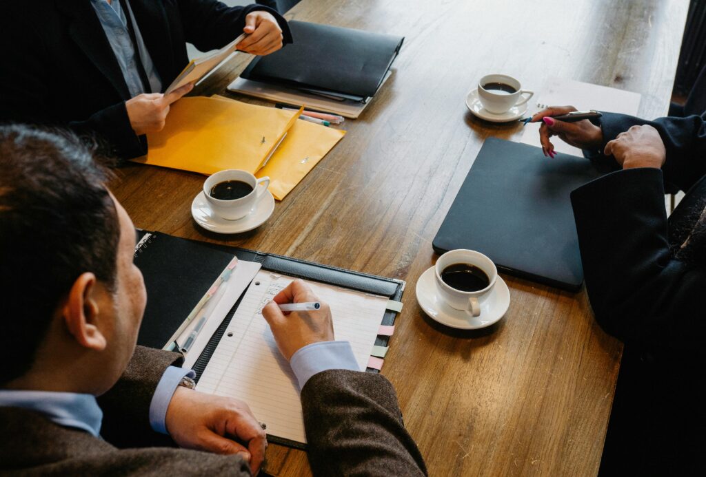 Business professionals engaged in a meeting at a wooden table with coffee and documents.