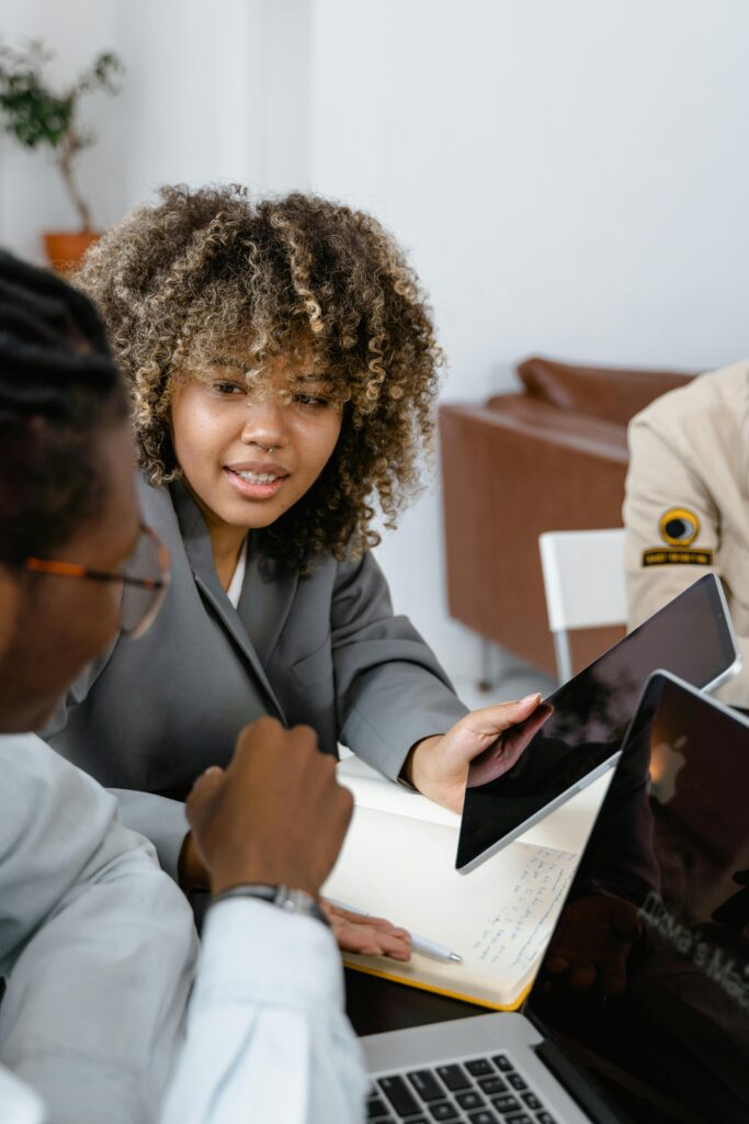 Team members engaged in a collaborative meeting with laptops and tablets in an office setting.